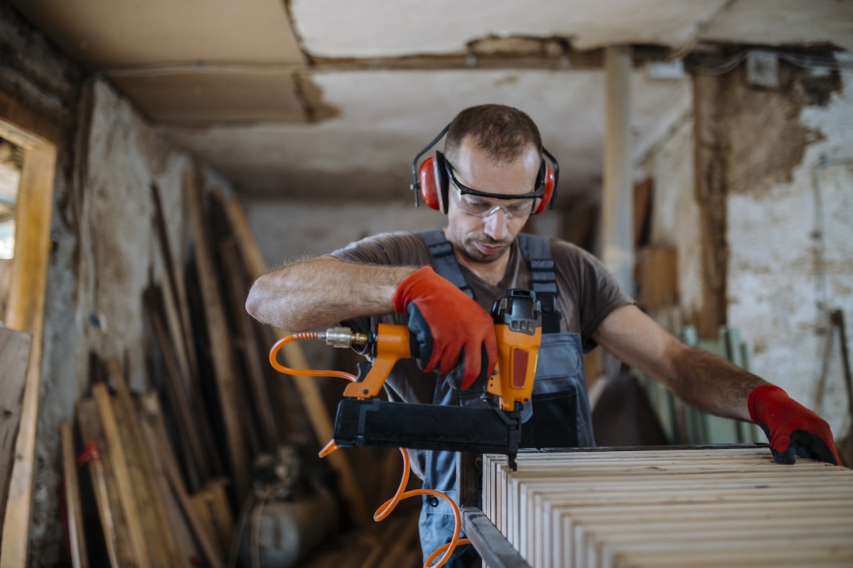 A man wearing PPE safely using a nail gun.