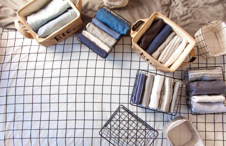 A woman folds her clothes and puts them in metal black baskets and boxes. Nordic style minimalism.