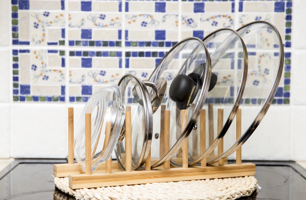 Glass pot lids on a wooden rack in front of blue and white tile kitchen backsplash.