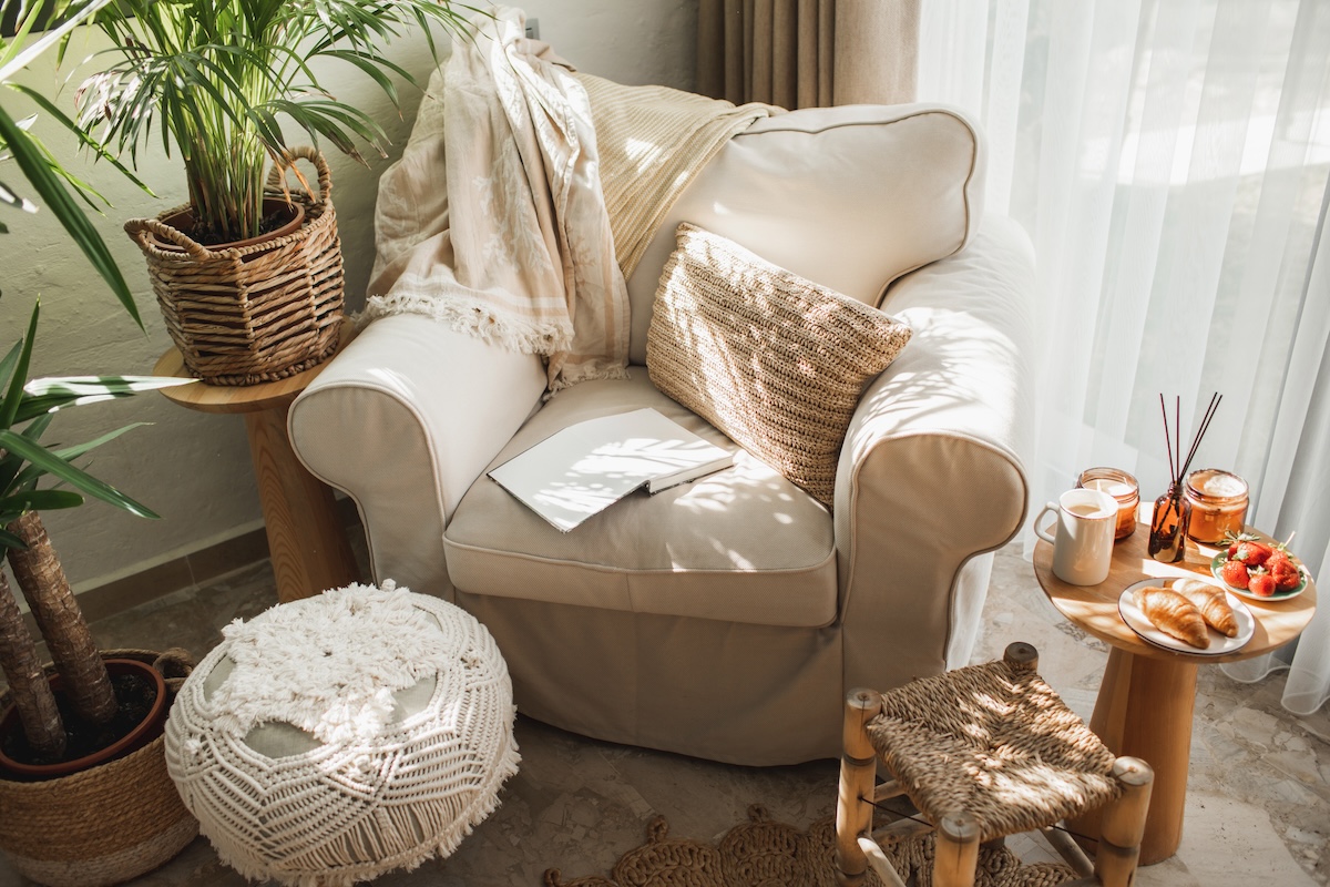 A large ivory-colored armchair with a matching crochet pouf ottoman, with house plants nearby.