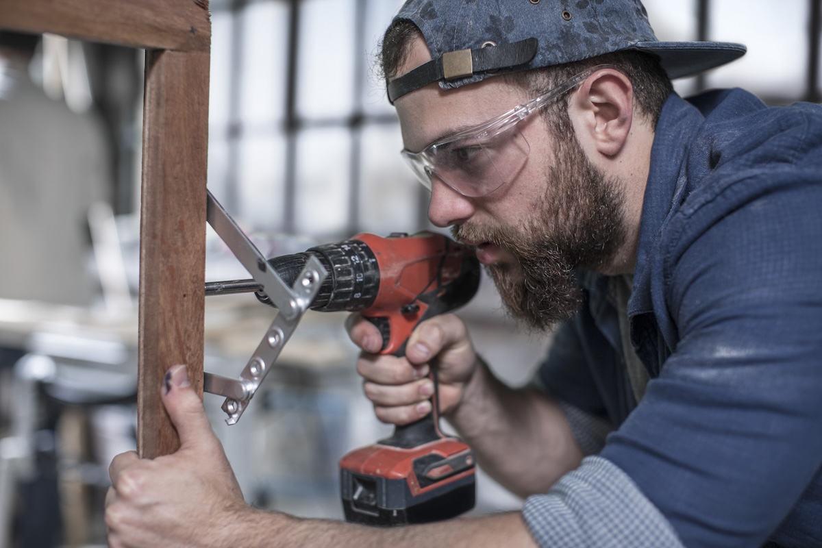 A man wearing eye protection while using a power drill.