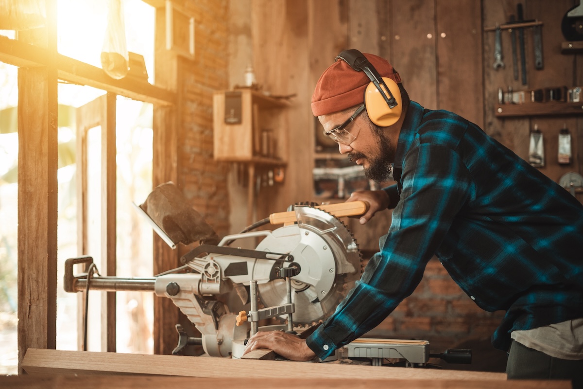 A man wearing personal protective equipment uses a table saw in his home workshop.