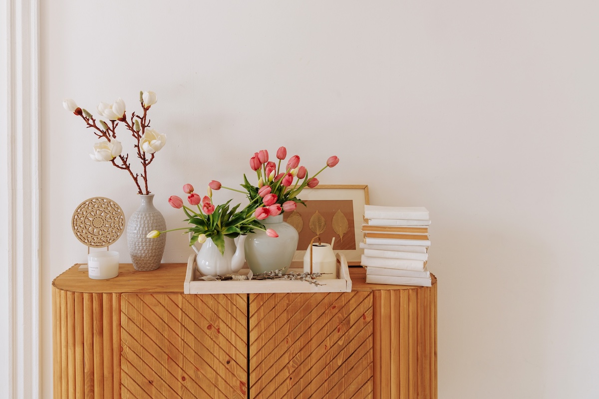 Simple home decor on a wooden hutch with a vase of tulips.