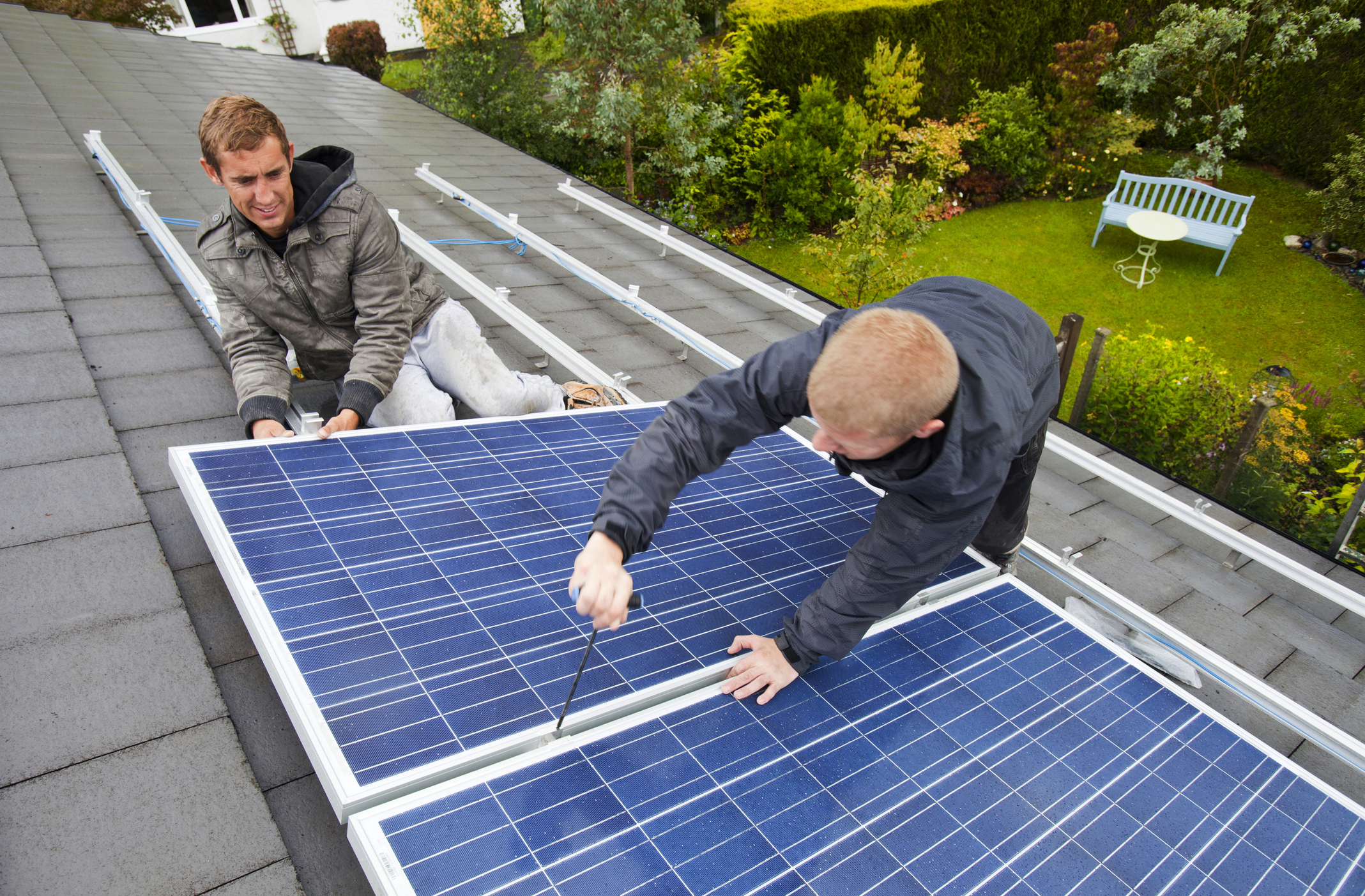 Technicians fitting solar photo voltaic panels to a house roof