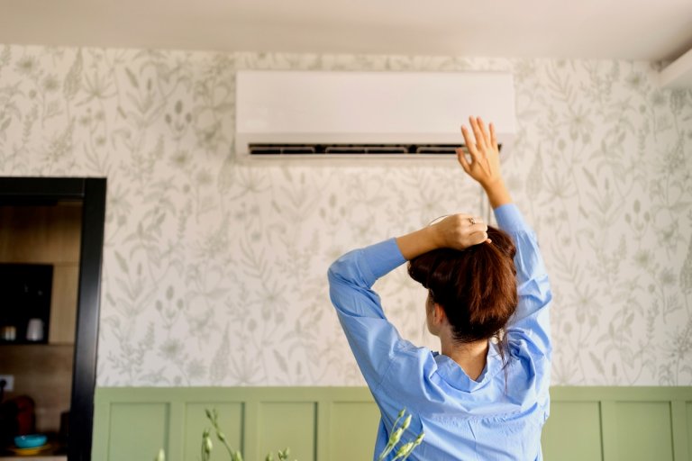 A homeowner feeling air coming from air conditioner during hot summer day.
