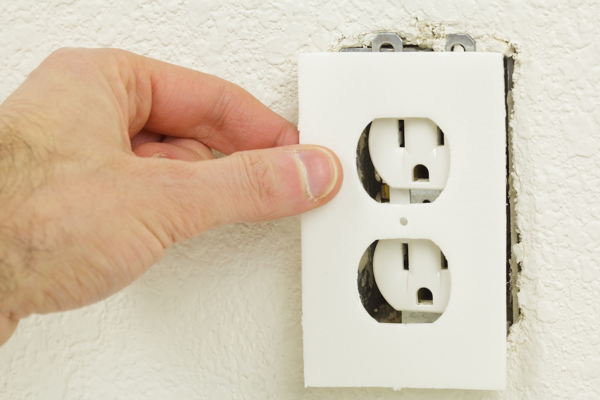 A person adding insulation behind wall outlet covers to keep a home cooler in summer months.