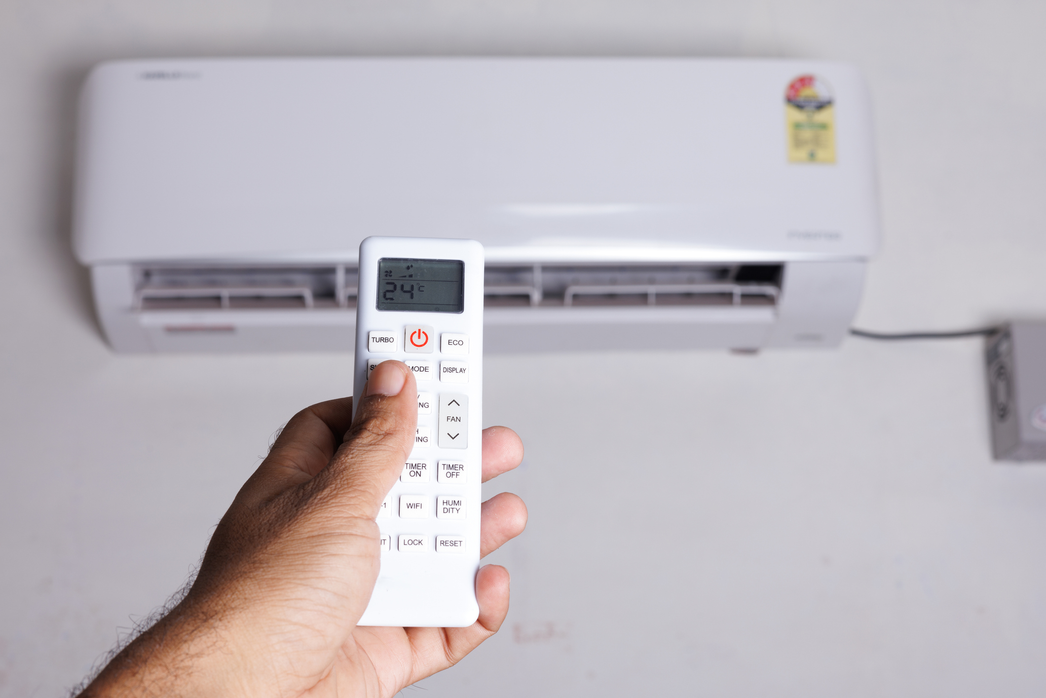 Man's hand with remote pointed at mini split AC unit on the wall.