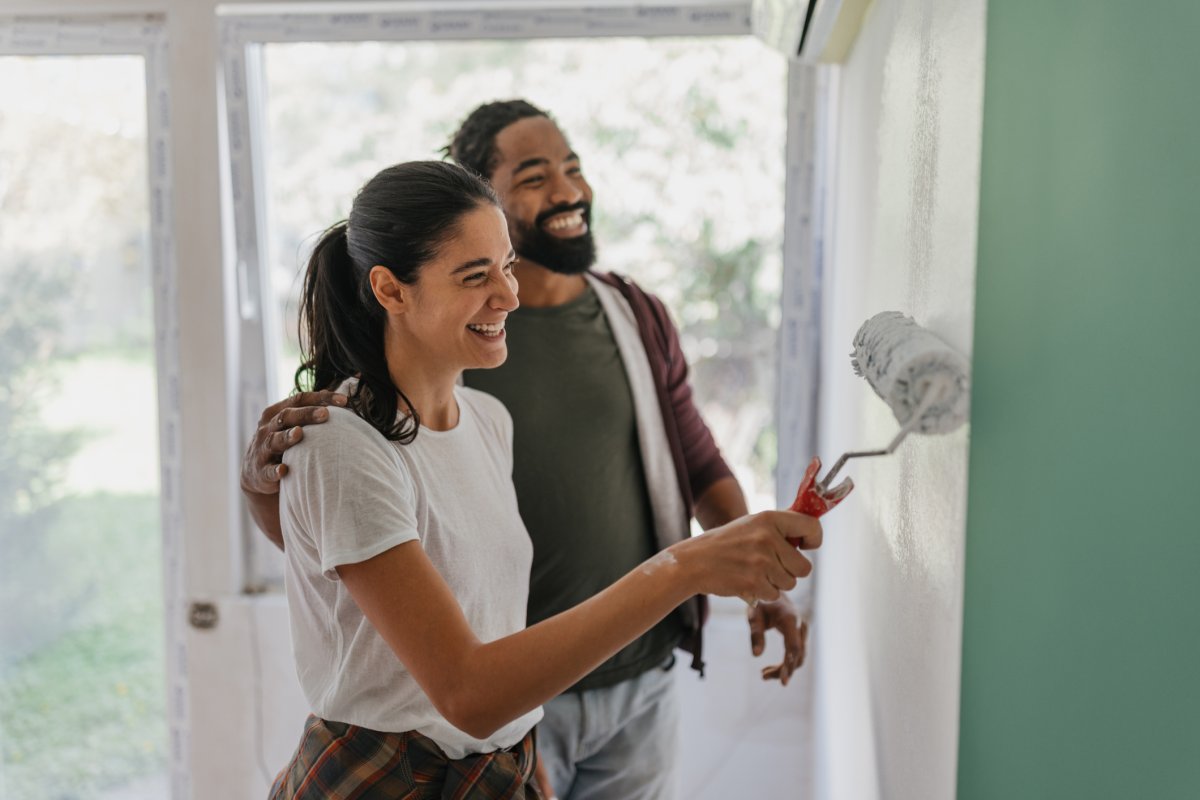Smiling couple paints a wall green in their home.