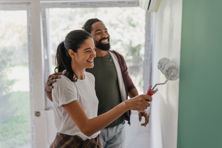 Smiling couple paints a wall green in their home.