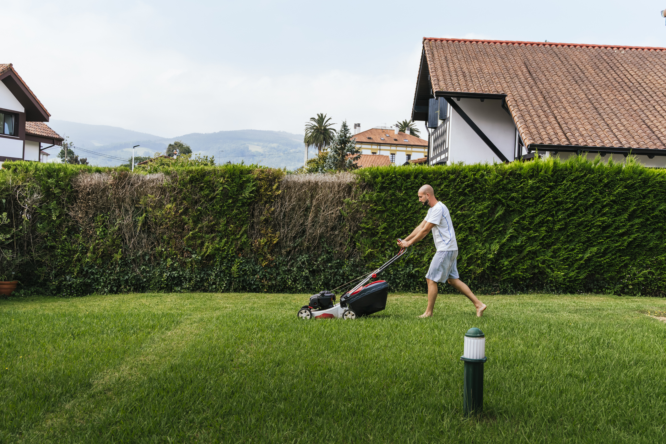 Man mowing grass with lawnmower with house next door in background