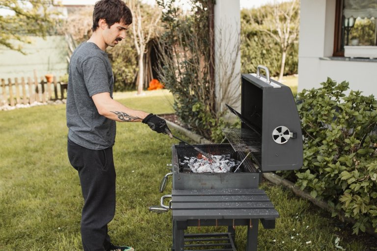 A man with a mustache pokes the ashes of a charcoal grill.