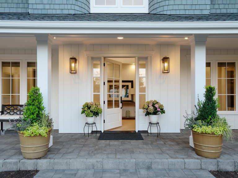A white home with a porch decorated with planters.