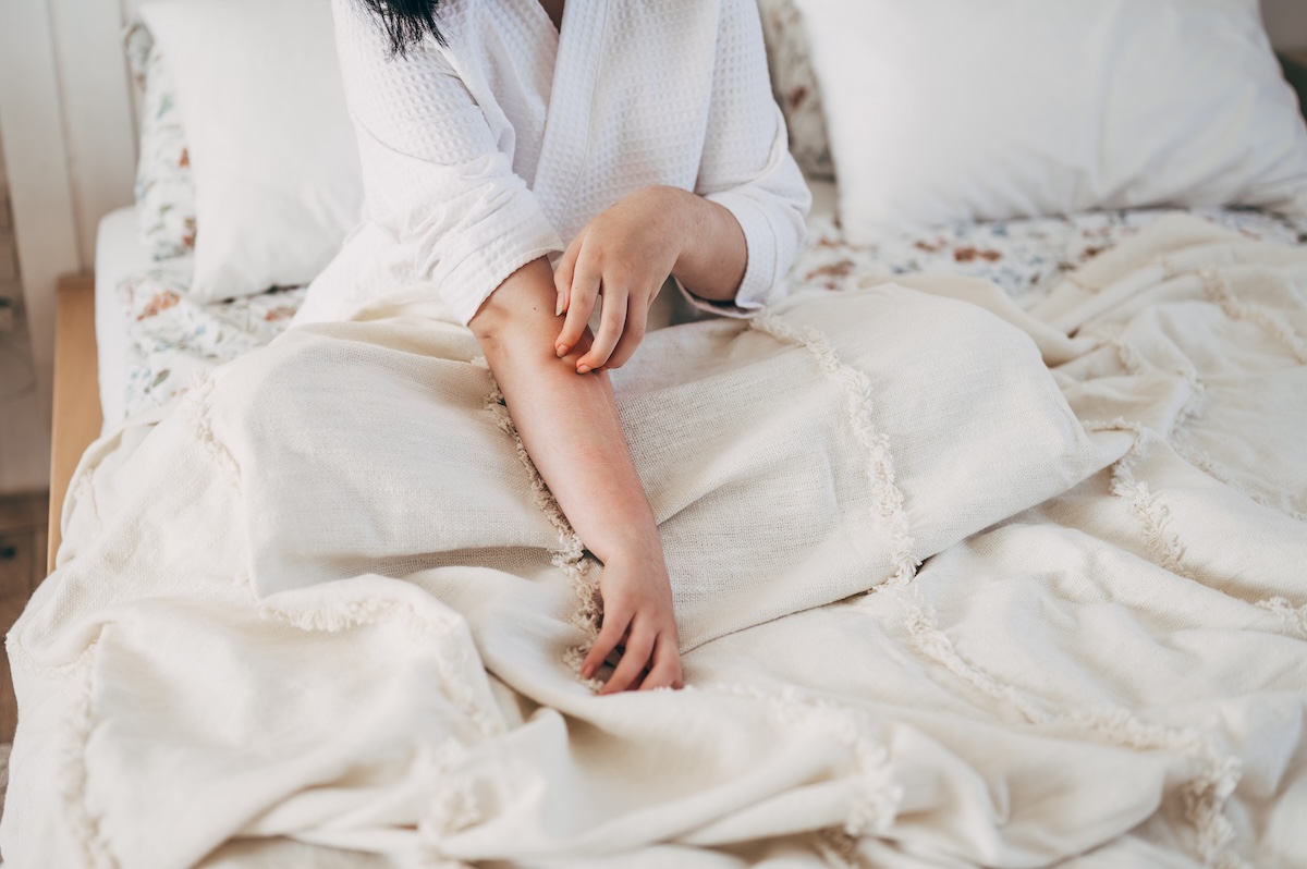 A woman scratches her dry skin while sitting in bed.