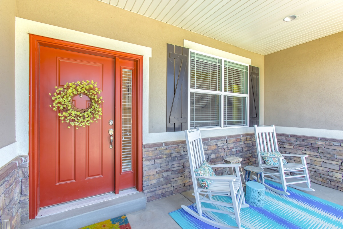 Home entry with a red front door with wreath and a bright blue outdoor rug and two chairs.