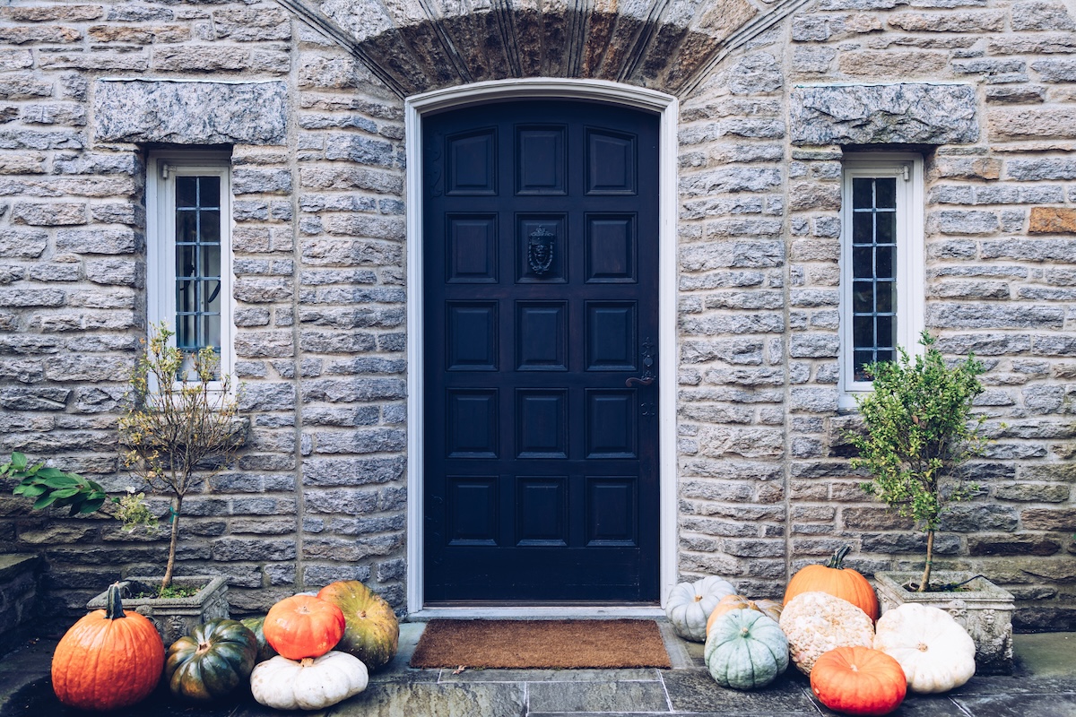A Navy blue front door with white painted trim and pumpkins on the stoop.