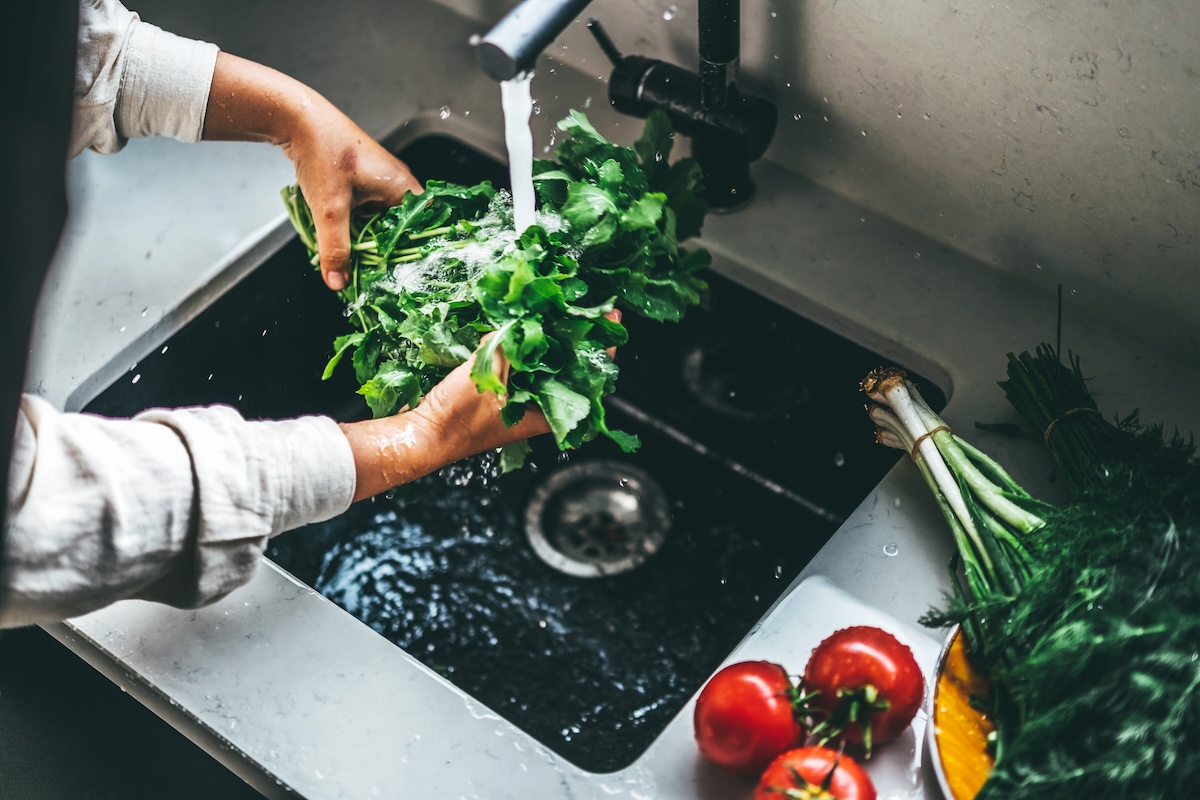 Hands rinse a bundle of green lettuce in a kitchen sink.