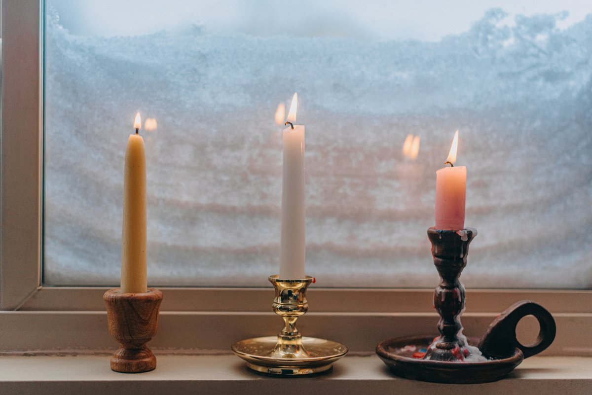 Three lit candles on a windowsill of a window covered in snow.