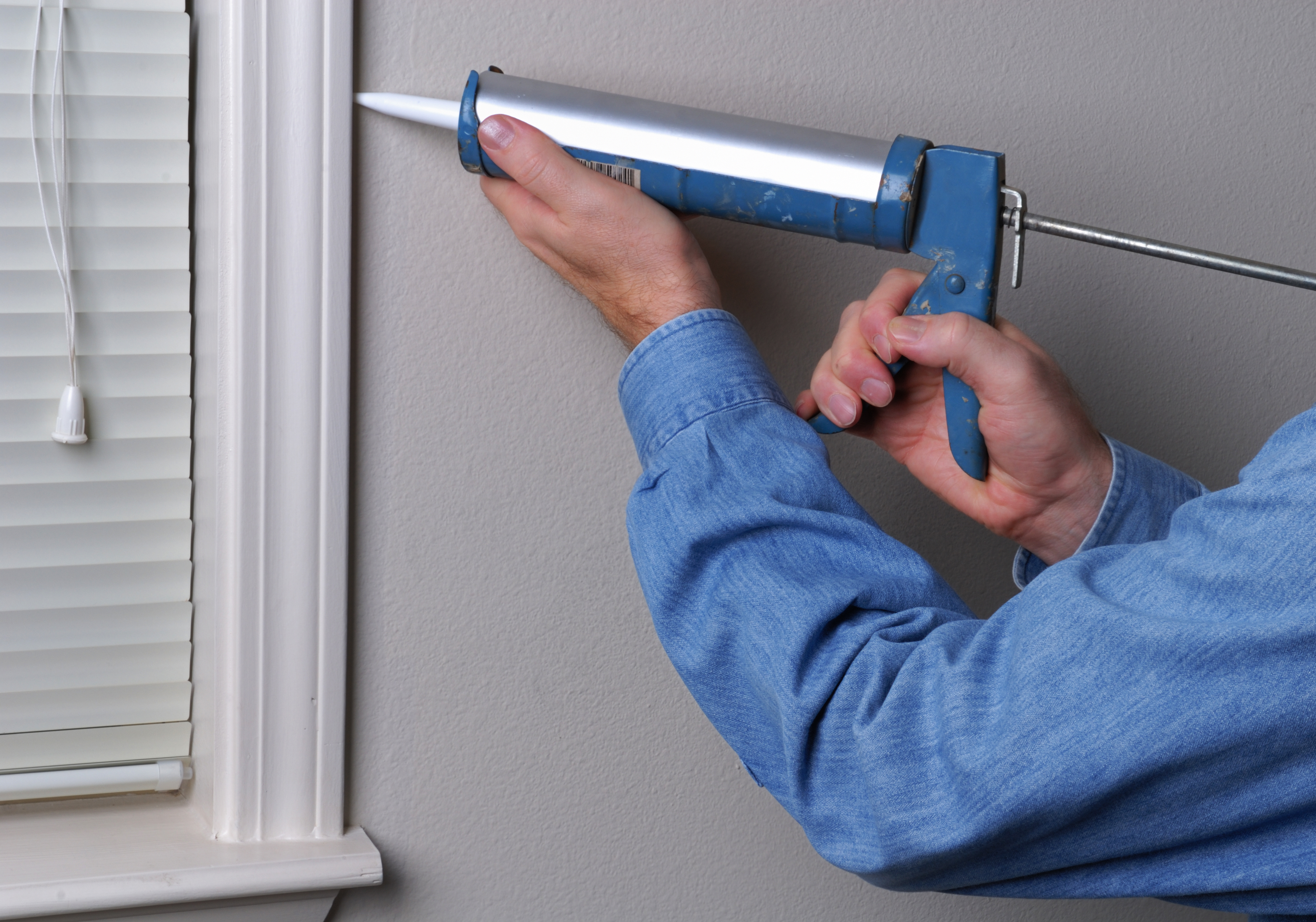 Caulking gun held by man's hand sealing window