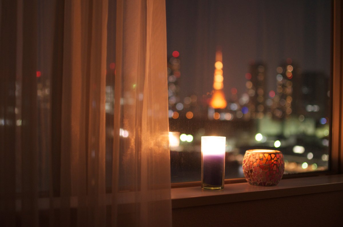 LIt candles on a windowsill at night with a city landscape in the background.