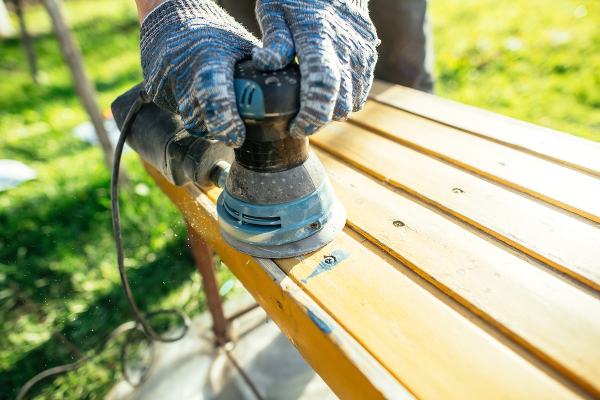 A person sanding wood furniture with a random orbit sander.