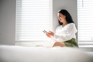 Woman on mobile phone sitting in front of bedroom window with cellular shades