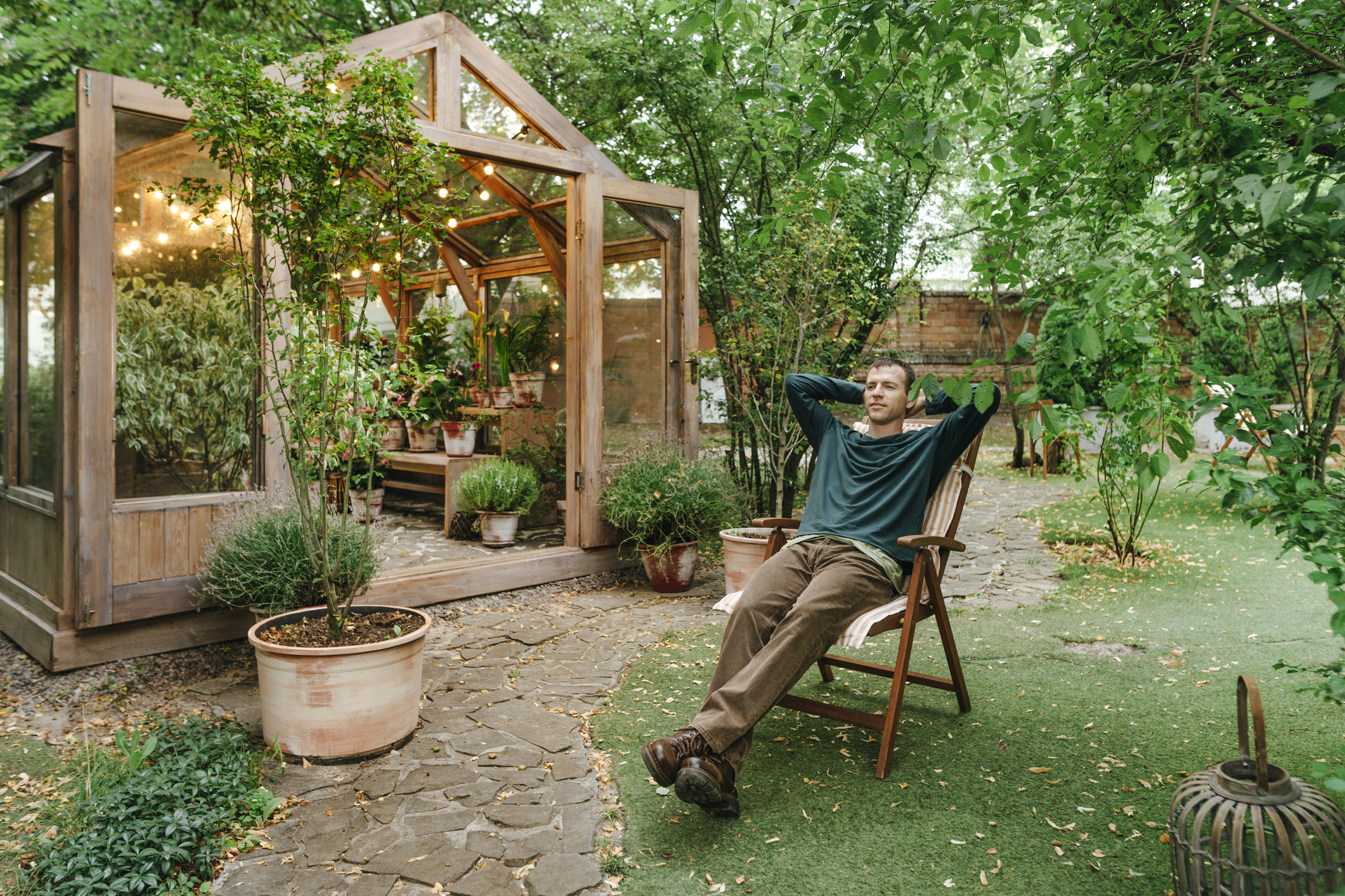 Man relaxing on deck chair in front of greenhouse in his backyard