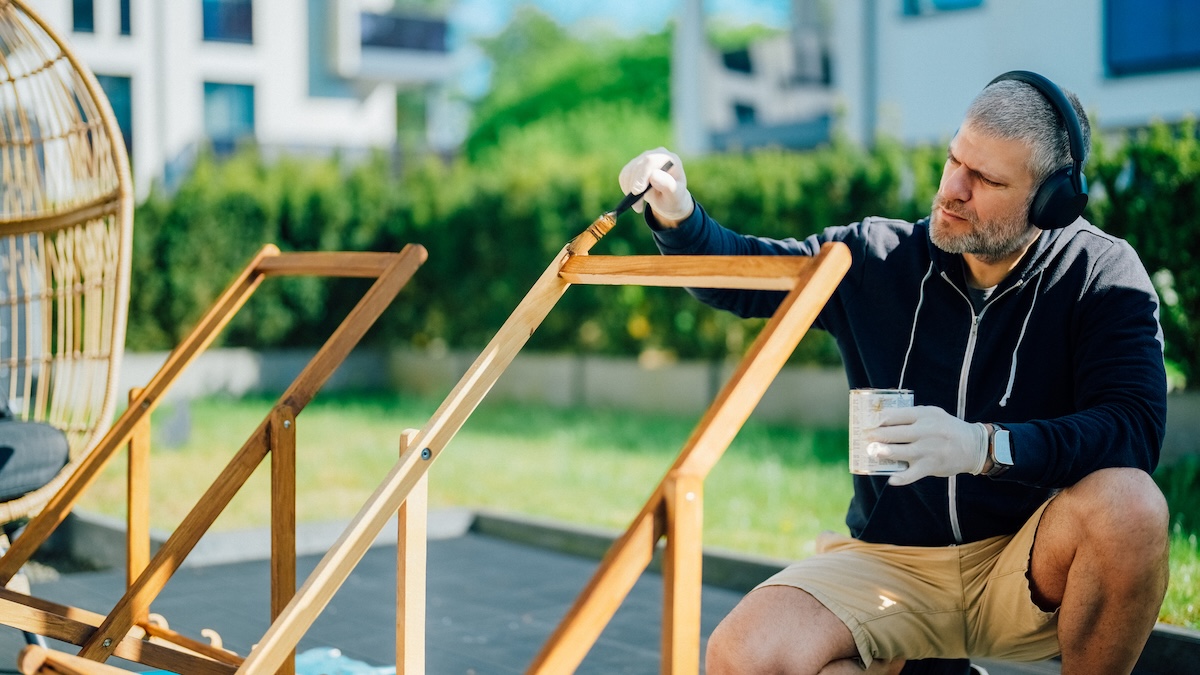 A person staining a wood chair outdoors.