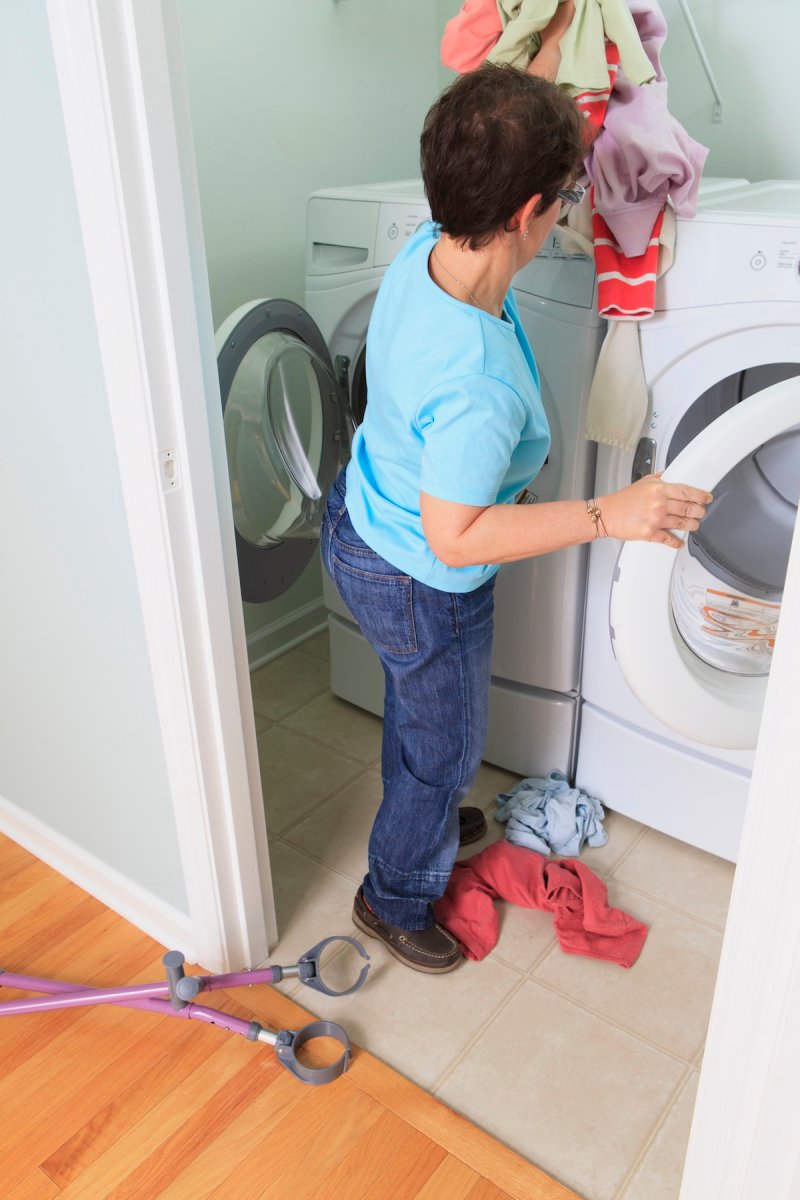 A person with walking crutches loading wet clothes into a dryer.
