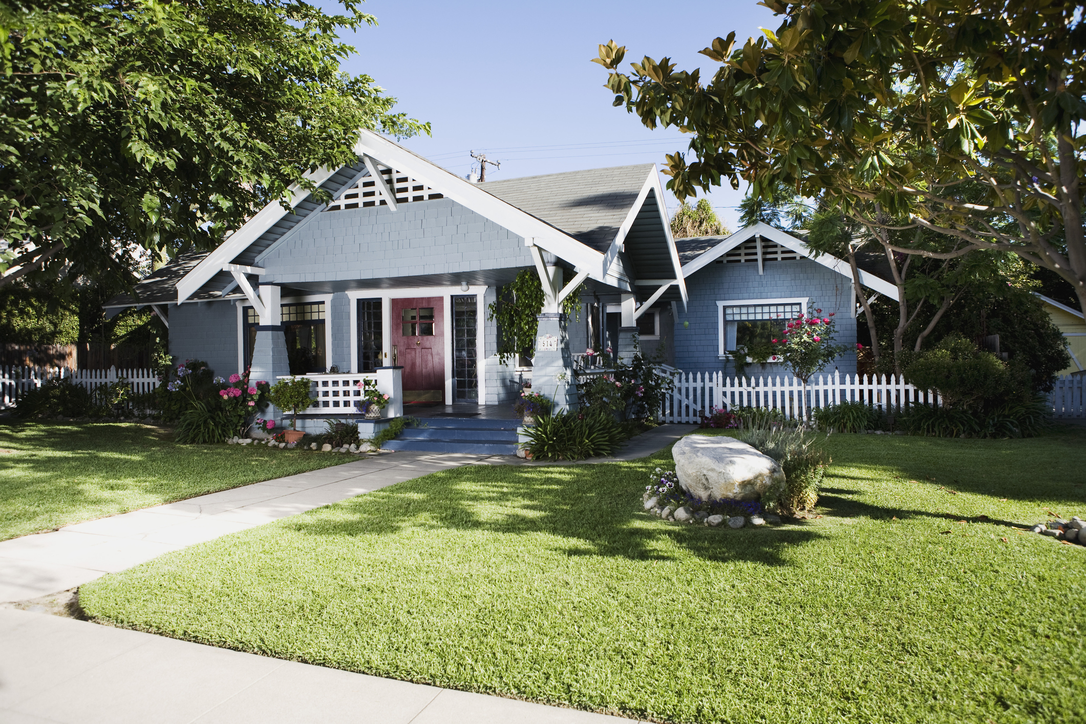 Blue Craftsman home exterior and front yard with a white picket fence
