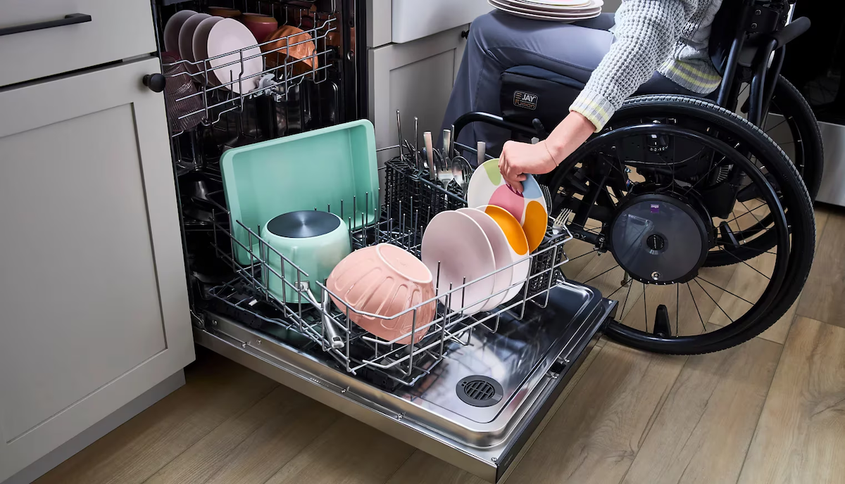A person in a wheelchair loading a dishwasher with a spinning lower rack for accessibility.