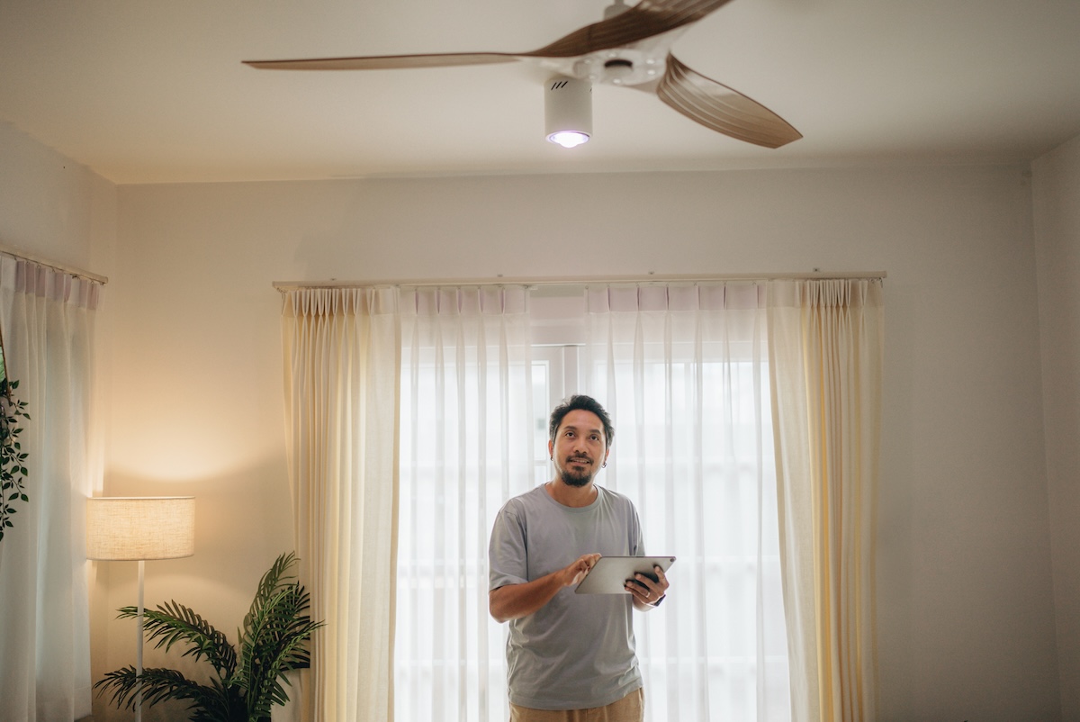 A man uses an electronic tablet to change the direction of a ceiling fan.