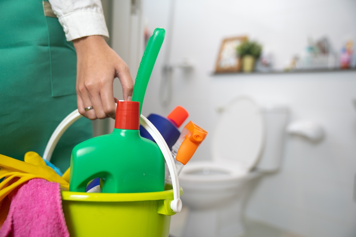 A person getting reach to clean the bathroom and toilet holding bucket of cleaning supplies.