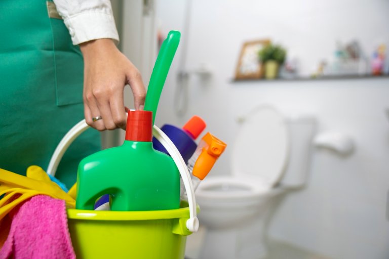 A person getting reach to clean the bathroom and toilet holding bucket of cleaning supplies.
