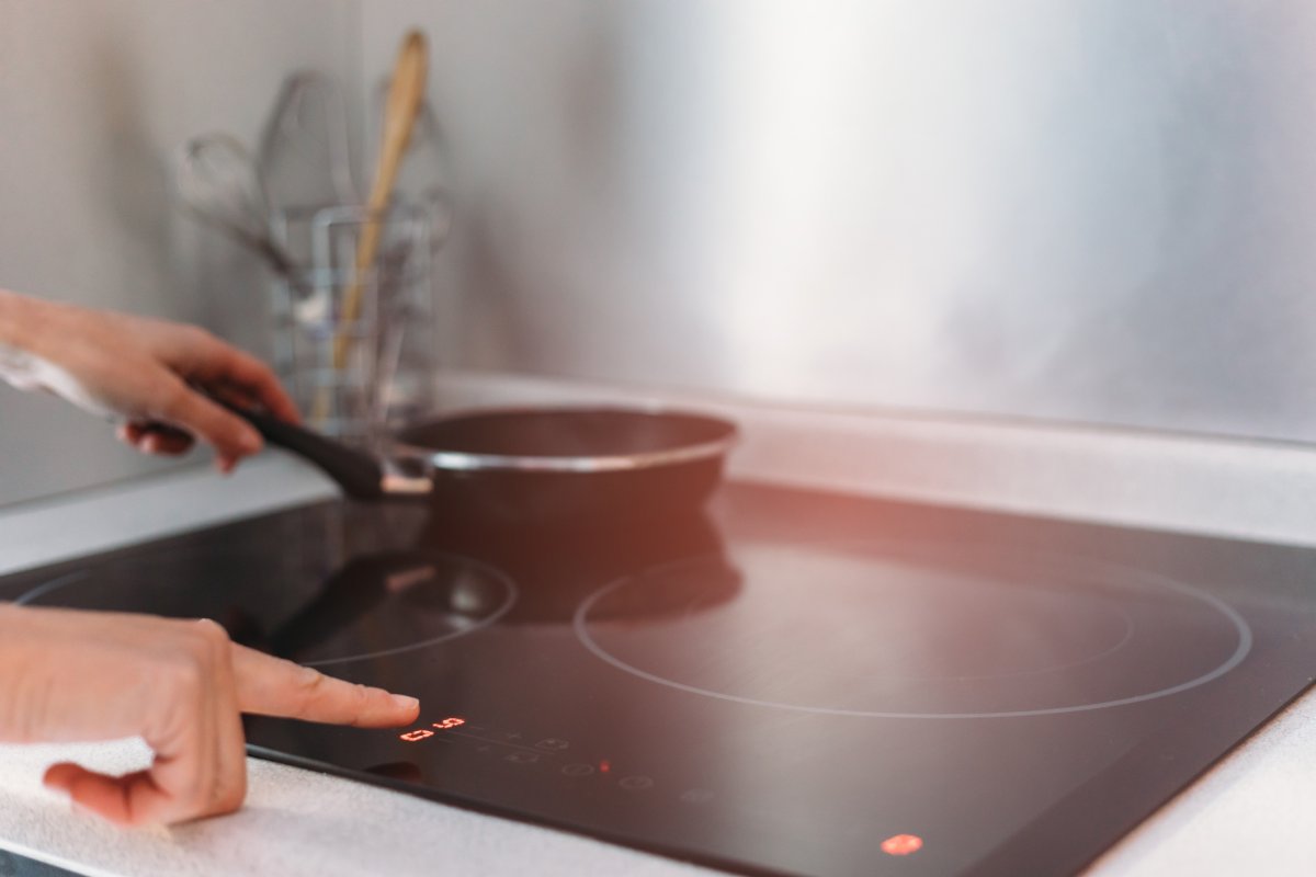 Detail of female hand using induction stove in kitchen and touching the touchscreen setting.