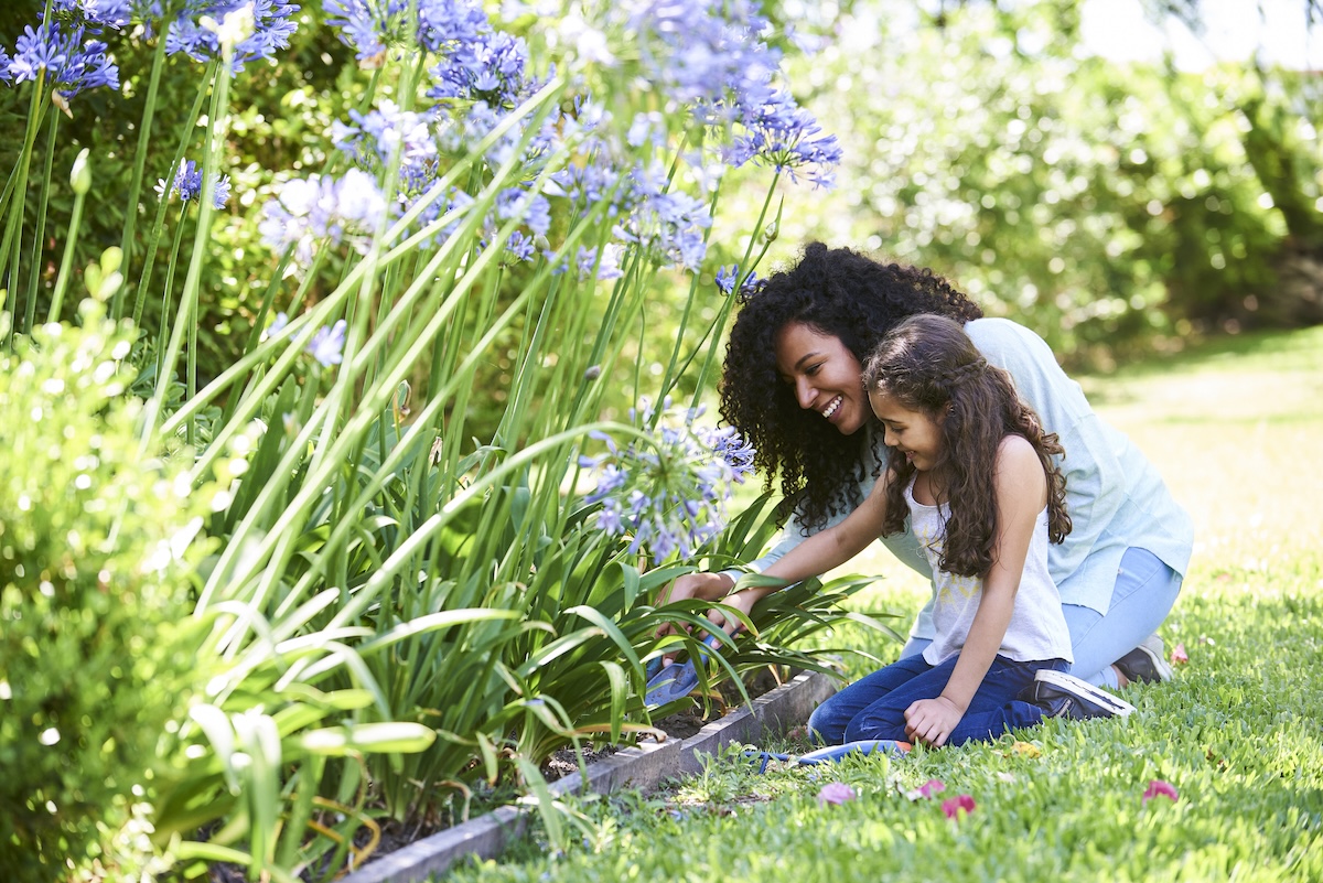 Mom and daughter using shovels in flower bed.