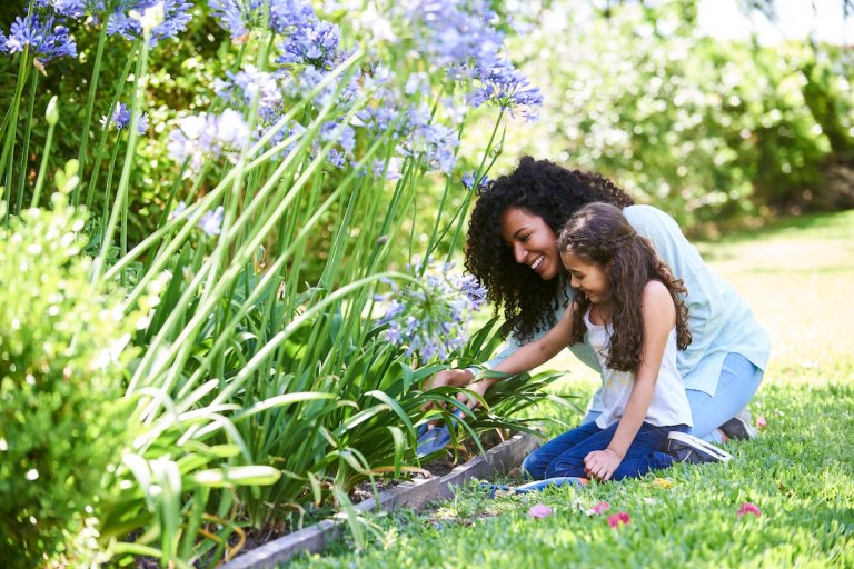 Mom and daughter using shovels in flower bed.