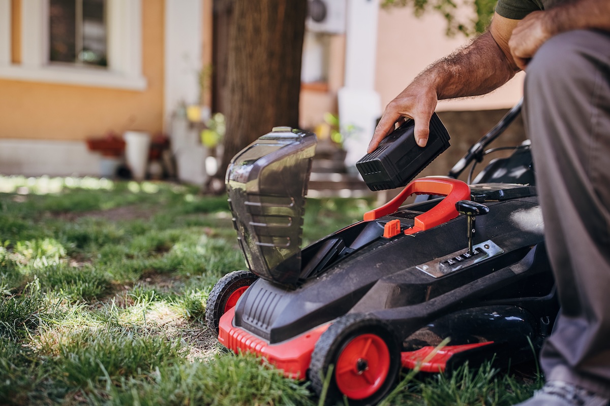A person adding a charged battery to an electric lawn mower.