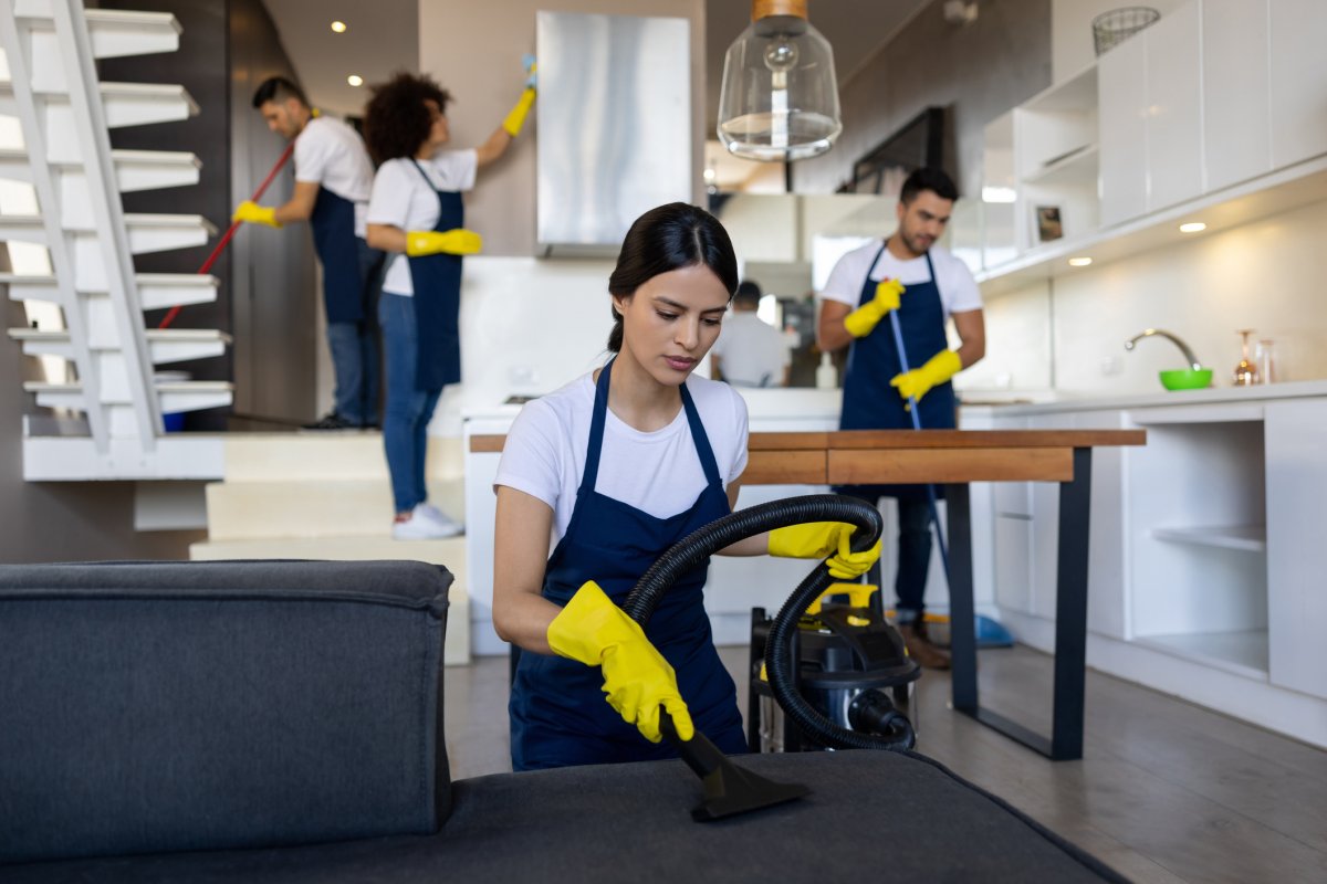 Professional cleaning crew vacuuming a couch and doing other cleaning tasks.