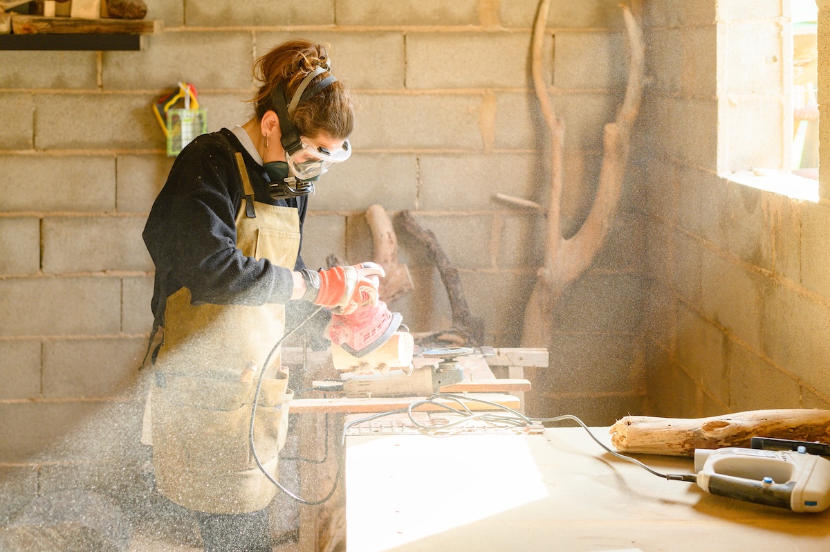 A carpenter working in a home workshop with a lot of dust, wearing eye and lung protection.