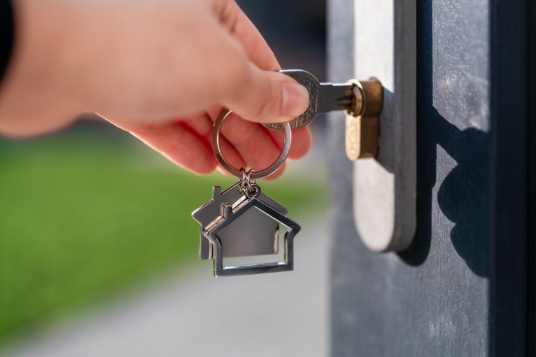 Close up of hand with key with a keychain in the shape of a house.