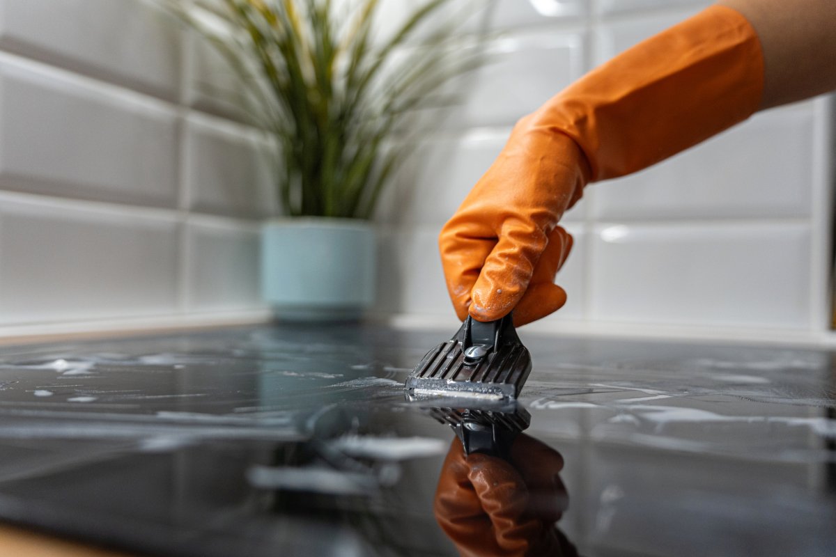 Closeup of an arm cleaning the glass-ceramic stove using a scraper tool.
