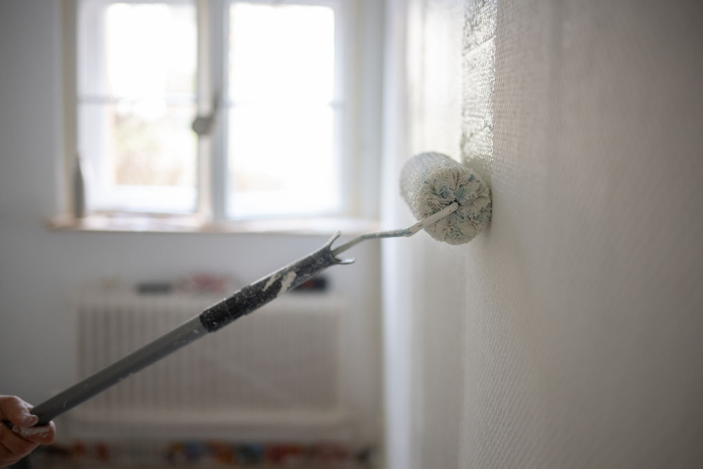 Paint roller adding a coat of white paint to the wall.