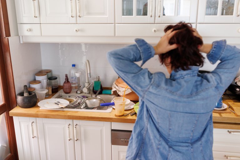 Woman holding her head while feeling stressed from the mess in the kitchen