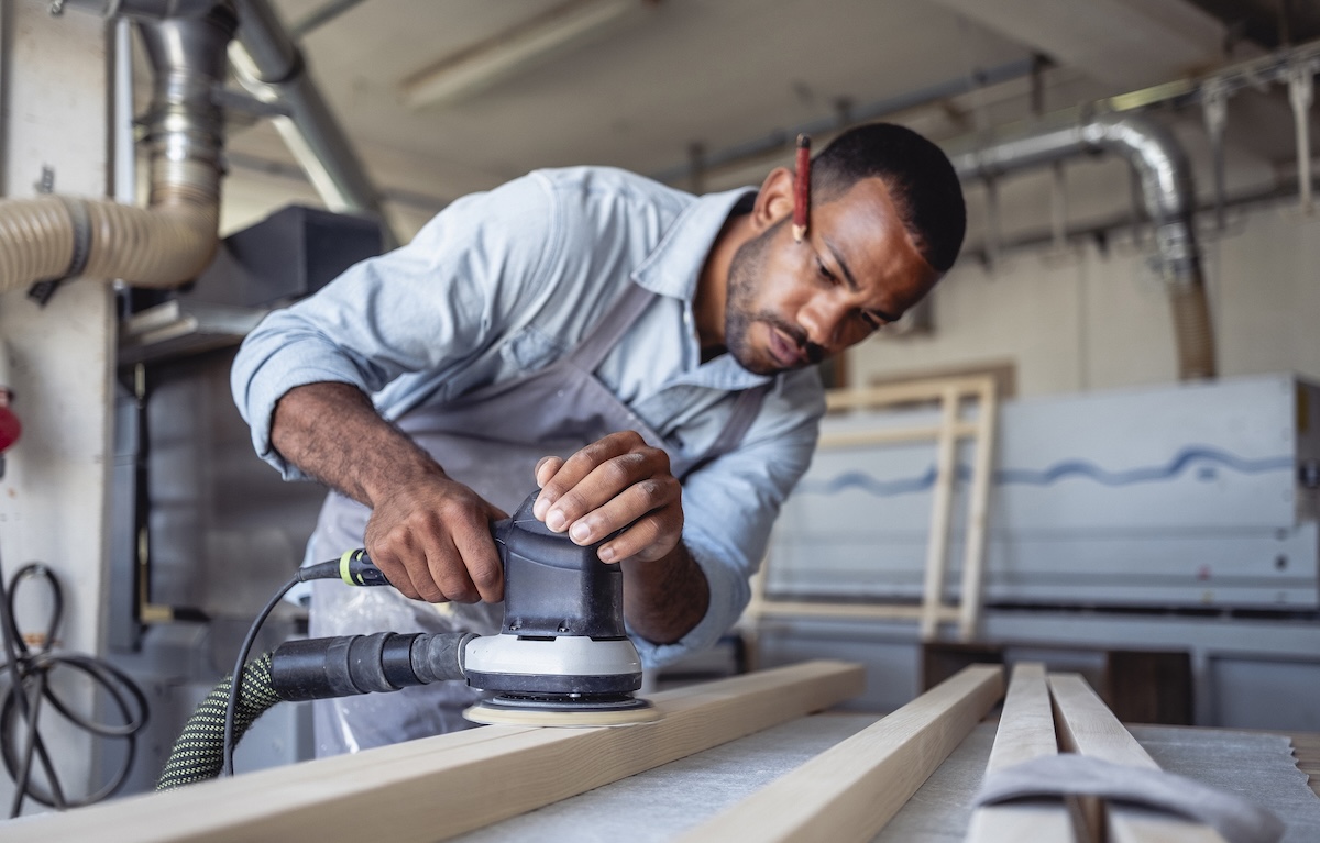 A DIYer using a sander with dust extraction in a home workshop.