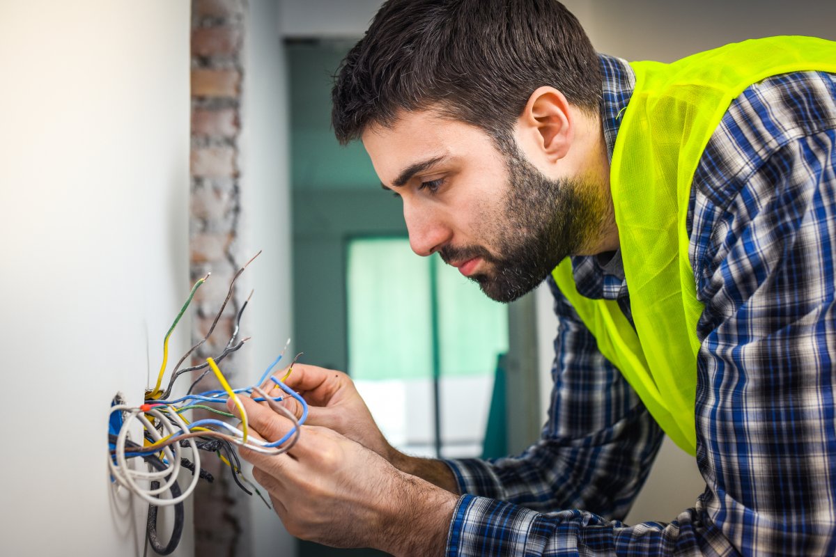 Electrician wearing a yellow vest connecting wires in the wall of a house