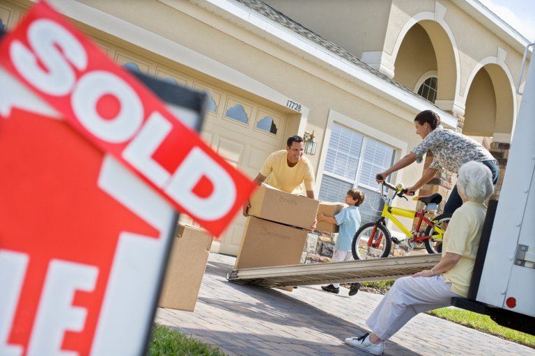 Family moving into a new house and carrying boxes and a bike off the moving truck