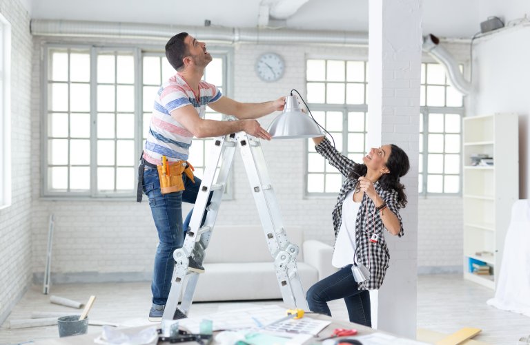 Couple hanging a light fixture in their home.