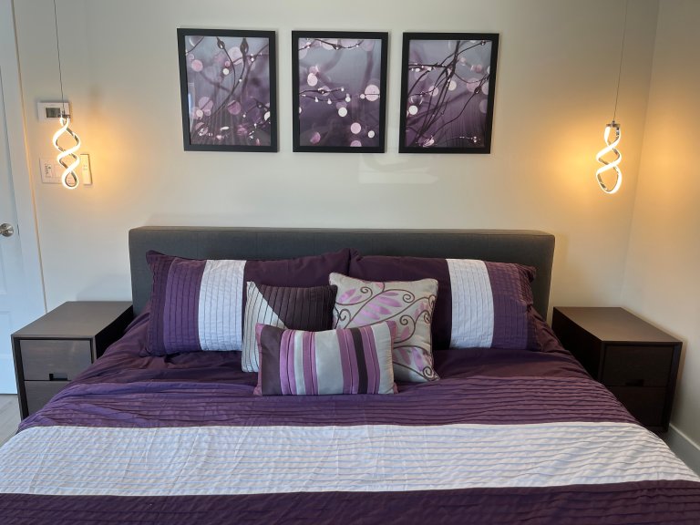 King size bed with gray fabric headboard, 2 hanging pendant lights glowing, and 2 dark wood skinny nightstands