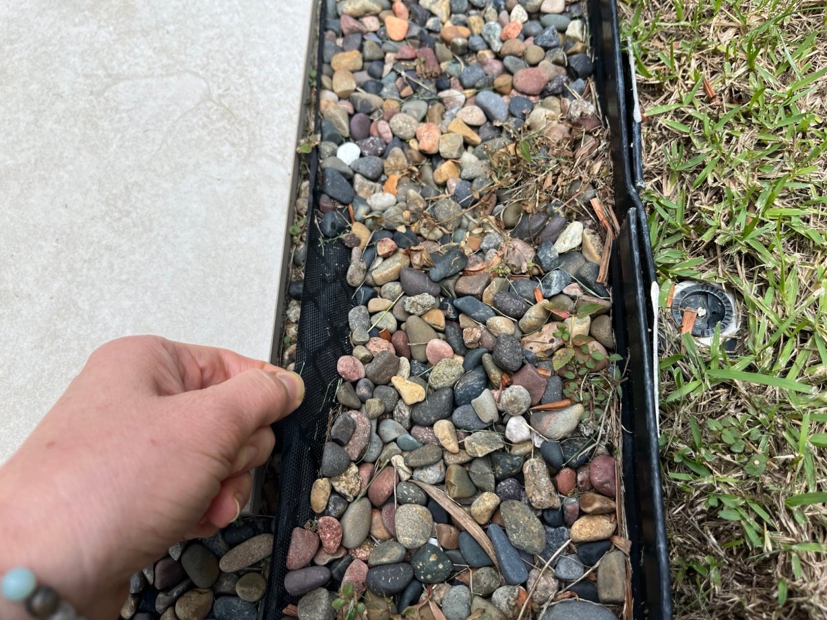 Close-up of hand pulling out landscape fabric next to pebbles and paver walkway