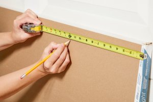 Hands marking a piece of drywall for cutting.